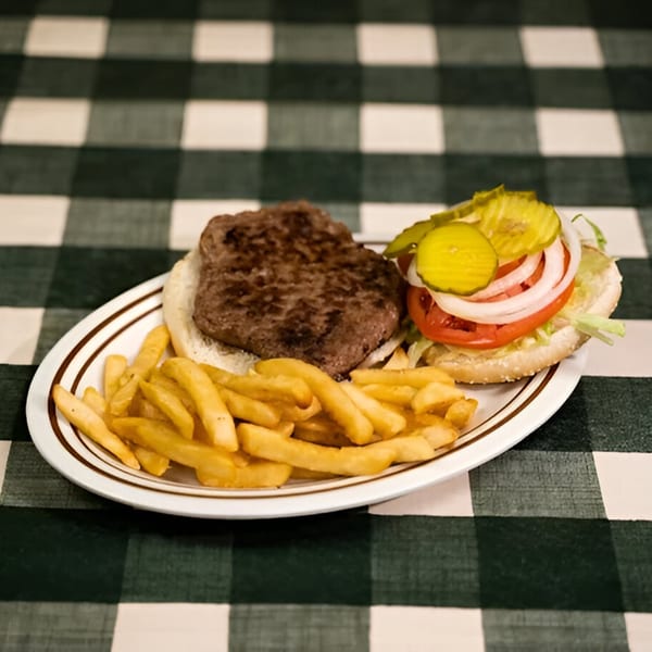 A classic diner hamburger with pickles, tomato, onion, and fries on a white plate with a checkered tablecloth.