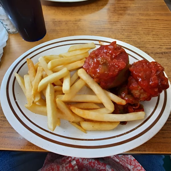 A diner plate with french fries and two meatballs covered in red sauce, with a drink beside it.