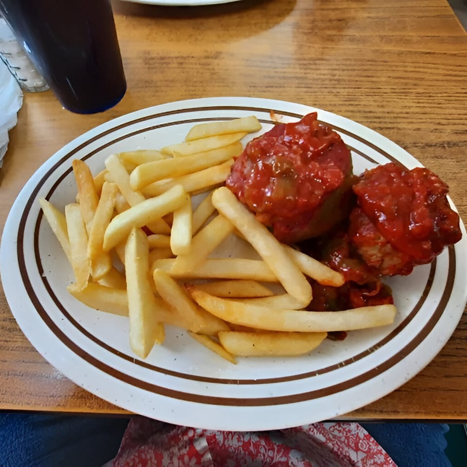 A diner plate with french fries and two meatballs covered in red sauce, with a drink beside it.