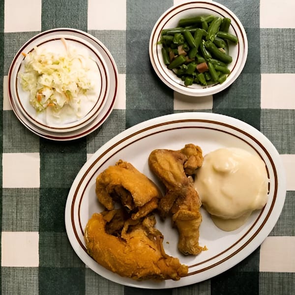 Studebaker's fried chicken, mashed potatoes, green beans, and coleslaw on a checkered tablecloth.