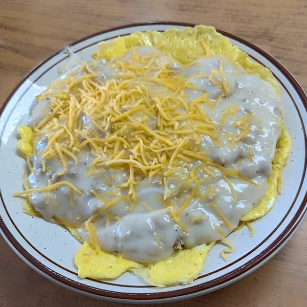 A diner breakfast plate with scrambled eggs, sausage gravy, and shredded cheddar cheese.