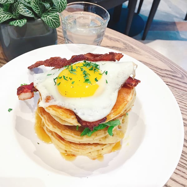 A stack of pancakes topped with bacon, a fried egg, and syrup on a white plate.