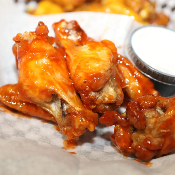 Spicy orange chicken wings with a side of ranch dressing on checkered paper at Studebaker's Country Restaurant.